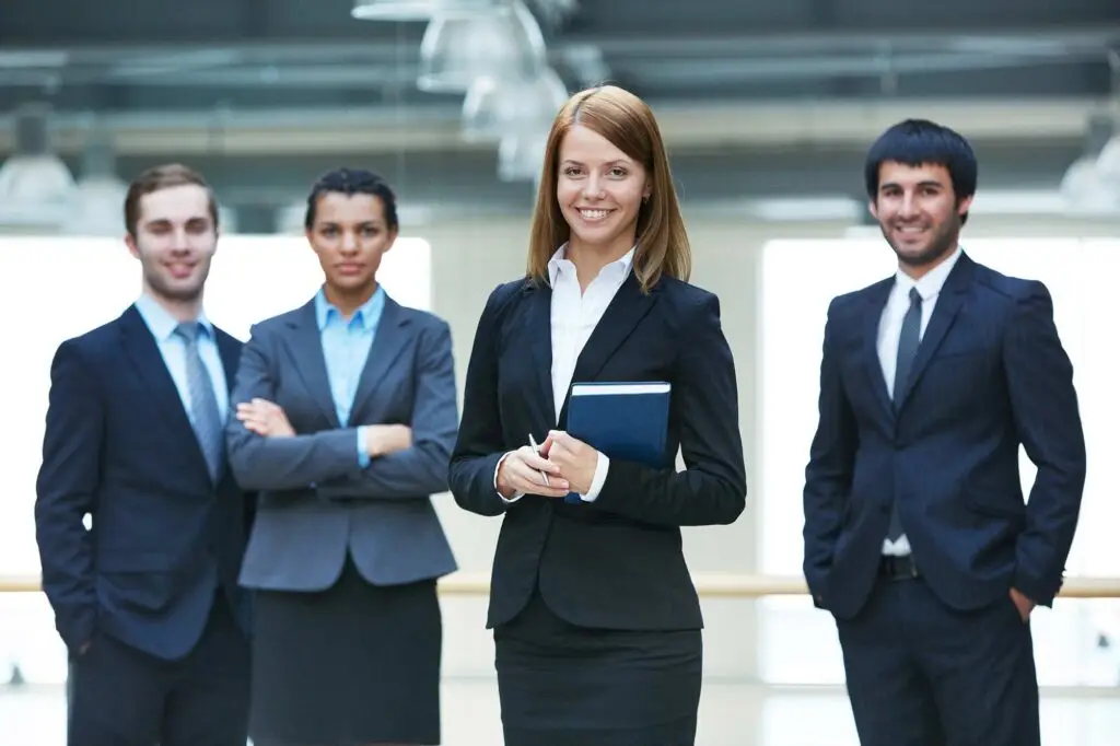Confident businesswoman standing with colleagues outdoors in professional attire.