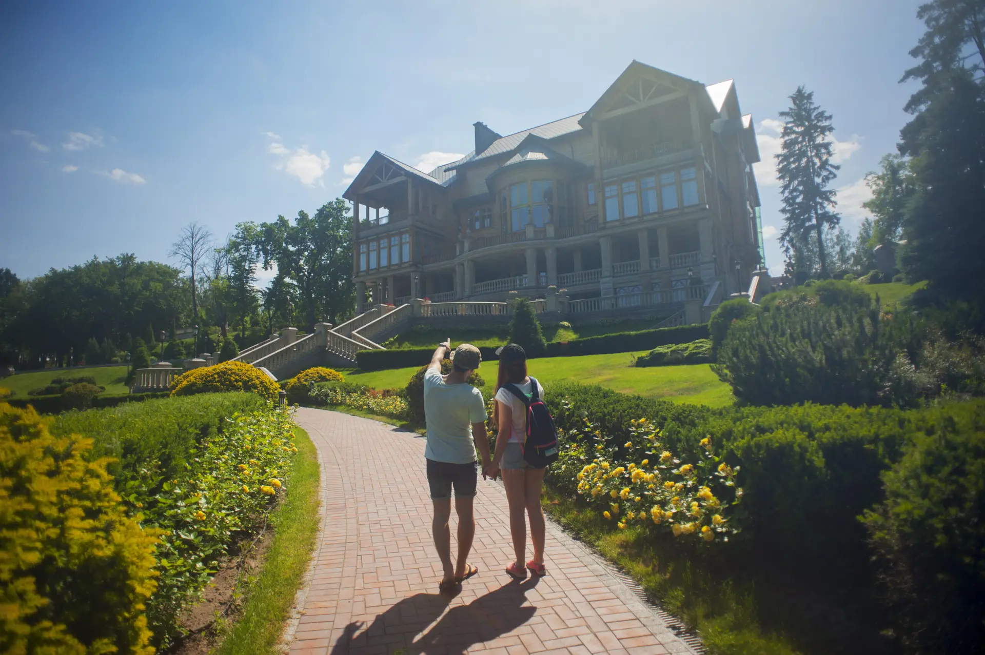 Two people walking on a pathway towards a large house on a sunny day.