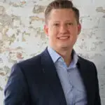 Professional man in a suit smiling against a world map background.