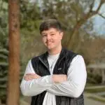 Young man standing outdoors with arms crossed, smiling.