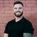 Smiling man with a beard and tattoo, wearing a black shirt.