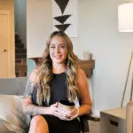 A woman with long hair sitting on a couch holding a glass of wine.