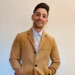 Young man in a tan coat smiling at the camera.