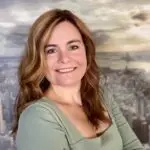 A smiling woman with wavy hair in front of a cityscape background.