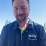 Man smiling, wearing a navy blue Seahawks polo shirt outdoors.