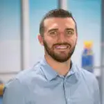 Smiling man with beard in light blue shirt indoors.