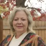 Smiling woman outdoors with autumn foliage and wooden fence background.