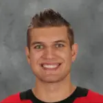 Portrait of a smiling young man with short hair and a red shirt.