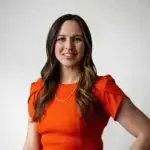 Young woman with long brown hair wearing an orange dress.