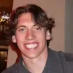 Young man smiling with medium-length hair indoors.