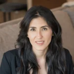 Professional woman with long dark hair smiling warmly indoors.