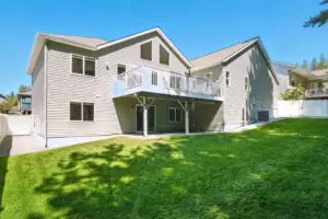 A large beige two-story house with a grassy yard and balcony.