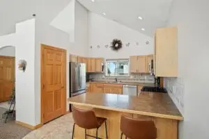 Modern kitchen with wooden cabinets, stainless steel appliances, and a breakfast bar with two chairs.
