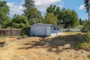 Small white shed in a grassy backyard with trees in the background.