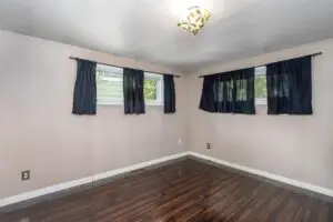 Empty room with wooden floor and windows with dark curtains.