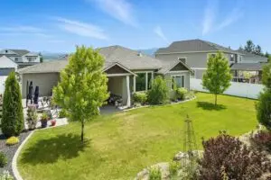 A single-story house with a large green lawn and trees under a blue sky.