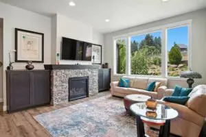 Modern living room with fireplace, TV, and large window overlooking greenery.