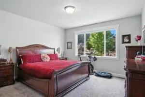 Cozy bedroom with wooden bed, red bedding, and a treadmill by the window.