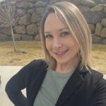 Smiling woman outdoors with stone wall background.