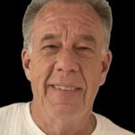 Elderly man smiling in white shirt.