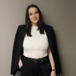 Woman in business attire against gray wall.